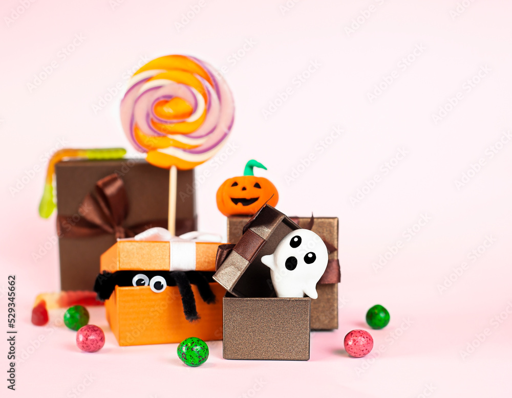 Obraz premium gift boxes with halloween symbols, lollipops and candies on a pink background close-up