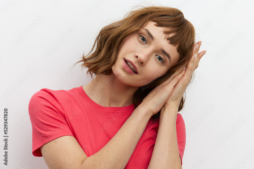 horizontal photo of a cute, attractive, laughing red-haired woman in a red cotton T-shirt standing on a white background and holding her hands near her face. horizontal photo of a cute, attractive, laughing red-haired woman in a red cotton T-shirt standing on a white background and holding her hands near her face.