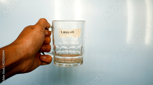 close up hand holding empty drinking glass with text word caffeine written on duct tape