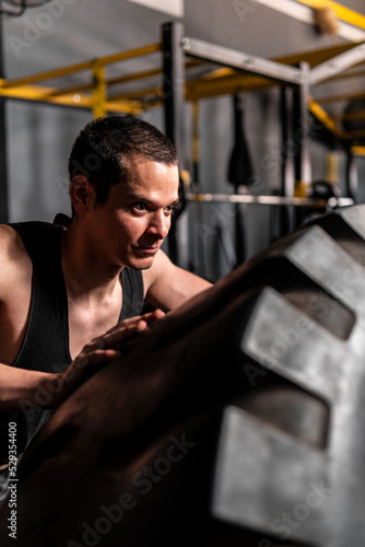 High quality photo. Short-haired man training in the gym. Very concentrated man pushing a giant tire in the gym. Man exerting effort when loading a tire. © Wacha Studio