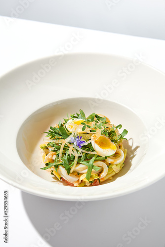 Healthy salad with squid and avocado on white plate with harsh shadows. Calamari salad with vegetables and eggs on white background with shadows of leaves. Summer food menu.