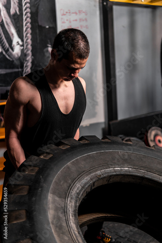 High quality photo. Caucasian man with short hair carrying a giant tire with great force. Strength training in the gym.