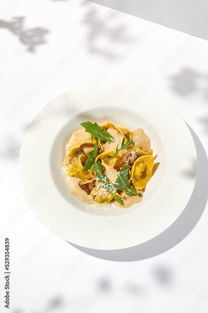 Italian ravioli with meat and mushroom sauce on white plate. Meat tortellini with creamy sauce in summer menu with shadows of tree leaves Ravioli stuffed beef in elegant style