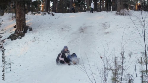 Young cheerful man and woman slide down the hill on flat sledges, winter activity, fun of sledding, slow motion