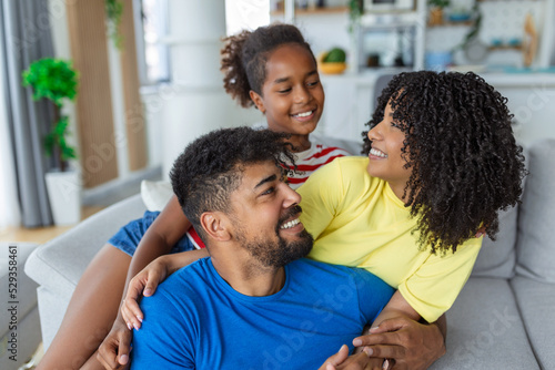Positive cheerful multi-ethnic family wife husband child sitting together on couch at home. Close up focus on little daughter and beautiful mother. Happy multiracial family concep © Graphicroyalty