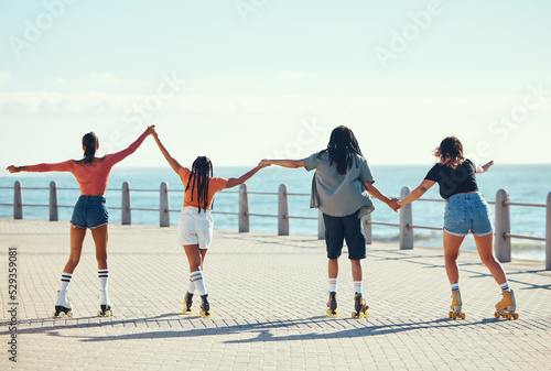 Roller skaters, friends and holding hands at a beach for exercise, fitness and freedom in summer together. Group, male and young girls skating on sidewalk at sea to relax on outdoor holiday vacation