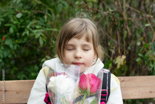 Portrait of a pretty girl sitting on a bench and holding a bouquet of roses