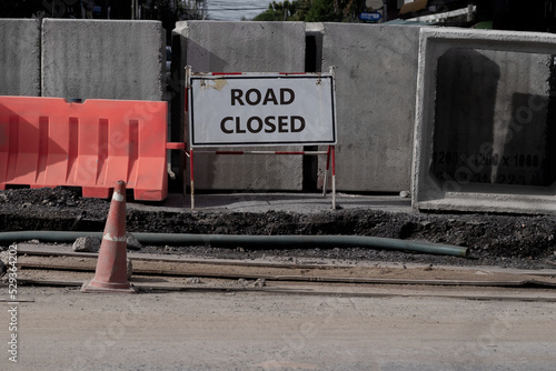 Under construction street with ROAD CLOSED word shown on white traffic signboard and group of concrete drainage tunnel block as barrior. Rough and grain textured of cement wall on uncompleted roadway.