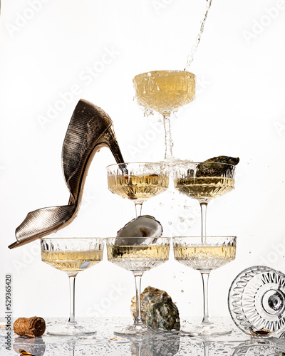 A large pyramid tower of champagne glasses alcohol cocktail with splash of berries oyster isolated on white background party with golden heeled shoe