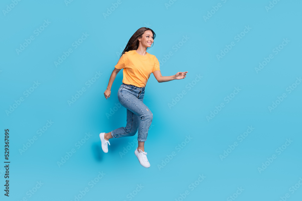 Full length photo of shiny sweet girl dressed yellow t-shirt jumping high running fast empty space isolated blue color background