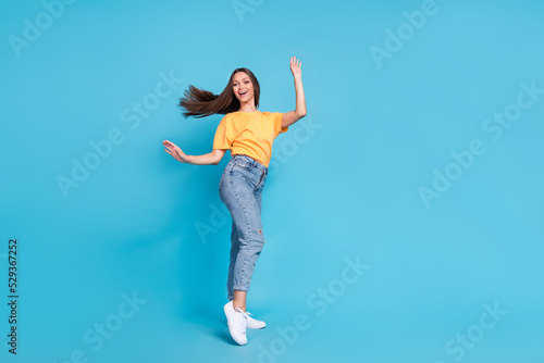 Full length photo of excited sweet girl dressed yellow t-shirt having fun dancing empty space isolated blue color background