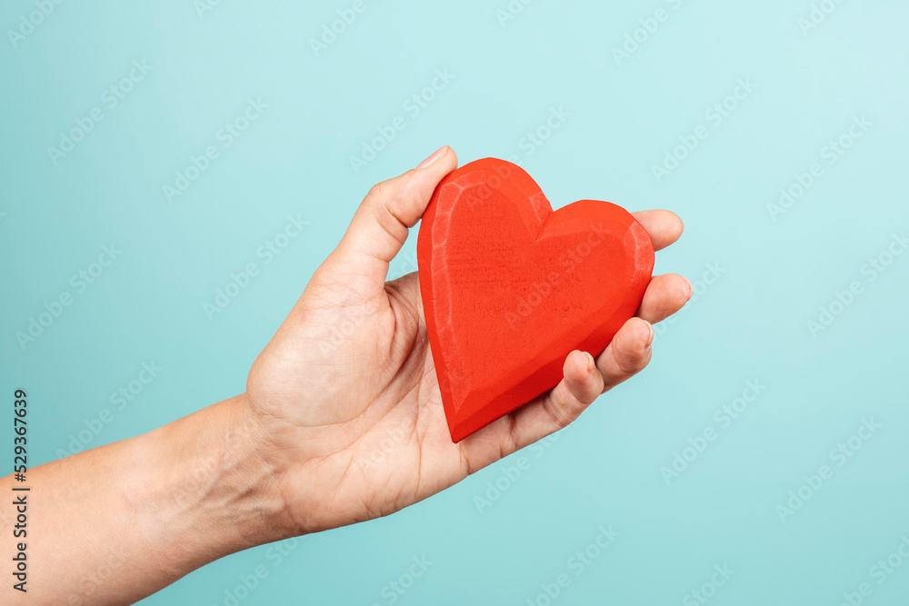 Woman hand holding red wooden heart on light blue background. Love, care, donation concept Woman hand holding red wooden heart on light blue background. Love, care, donation concept
