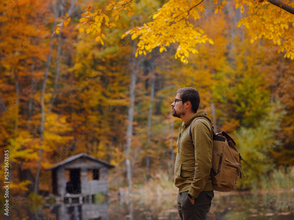 Young handsome man posing in autumn forest near lake. young hipster guy with backpack , traveller standing in woods, Hiking, Forest, Journey, active healthy lifestyle, adventure, vacation concept. Young handsome man posing in autumn forest near lake. young hipster guy with backpack , traveller standing in woods, Hiking, Forest, Journey, active healthy lifestyle, adventure, vacation concept.