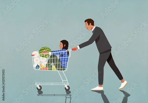 Father pushing daughter and groceries in shopping cart photo