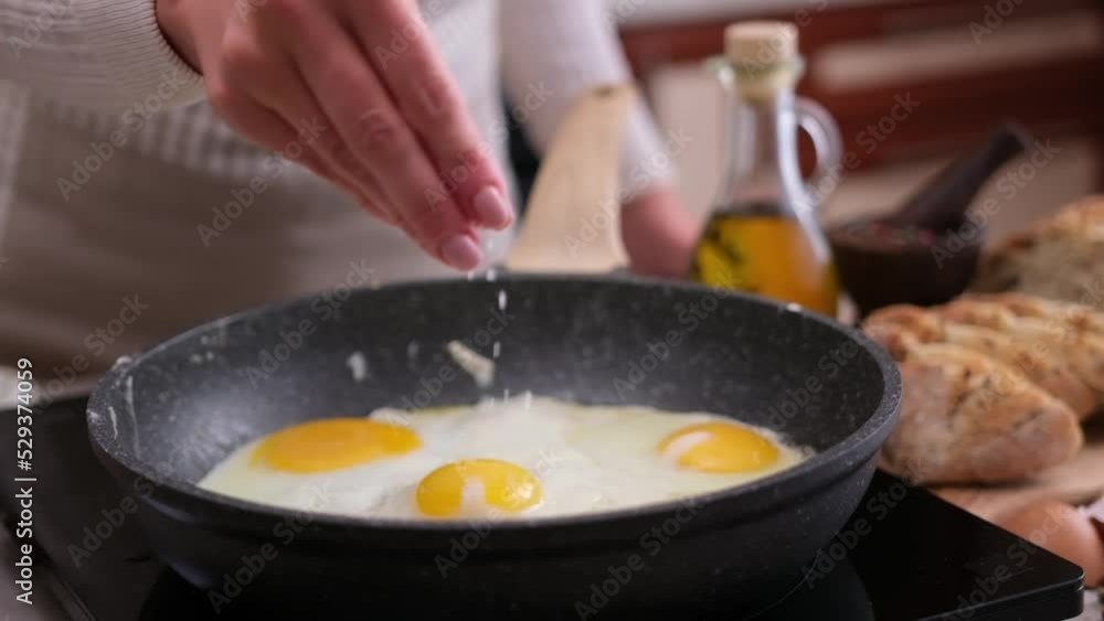 Woman salting fried eggs in a Non-stick pan on a stove Woman salting fried eggs in a Non-stick pan on a stove