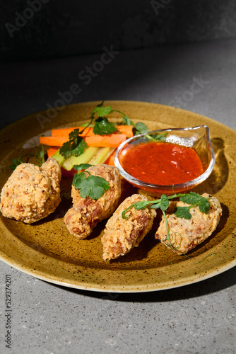 American appetizers buffalo wings with vegetables and sauce on gray stone table. Beer appetizer - Bbq wings on concrete background with hard shadow. Dark menu for pub. Chicken wings. Junk food.