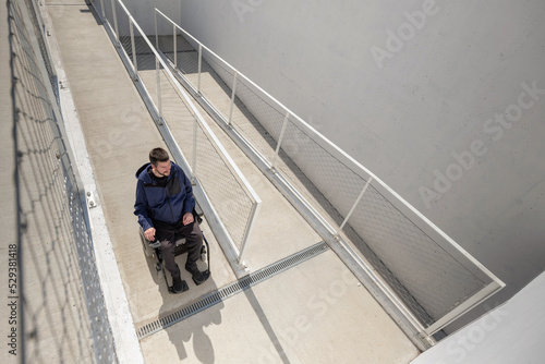 Man on wheelchair, approaching the building moving along an accessible ramp for persons with disability