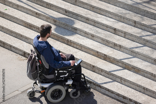 Person with disability on electric wheelchair stopping at the bottom of inaccessible staircase, unable to reach the top