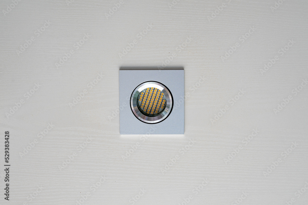 Energy saving LED spotlight in aluminum housing in white wooden ceiling with yellow diodes Energy saving LED spotlight in aluminum housing in white wooden ceiling with yellow diodes