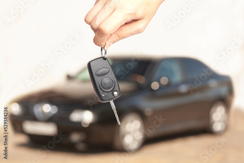 Car key in woman's hand with a car blurred in the background