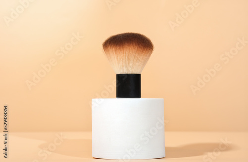 cosmetic brush for powdred or blush application on white geometric podium. cosmetic accessories, make up professional tools. photo