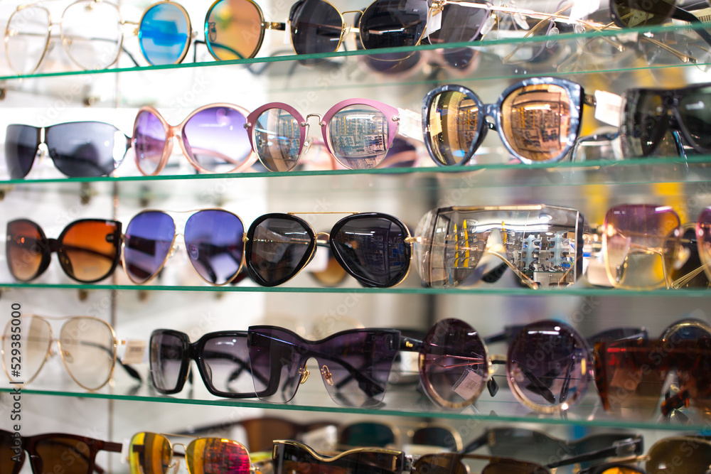 Sunglasses on optics shelves. Large selection of glasses for vision  correction. The glasses are laid out on the store's glass shelves in neon  lighting. foto de Stock | Adobe Stock