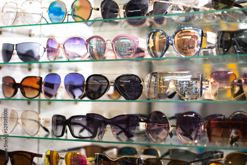 Sunglasses on optics shelves. Large selection of glasses for vision correction. The glasses are laid out on the store's glass shelves in neon lighting. © Vera