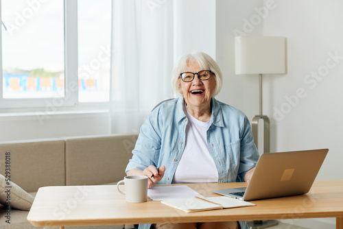 Intelligent elderly gray-haired businesswoman using a laptop at home. Senior online teacher conducts lecture