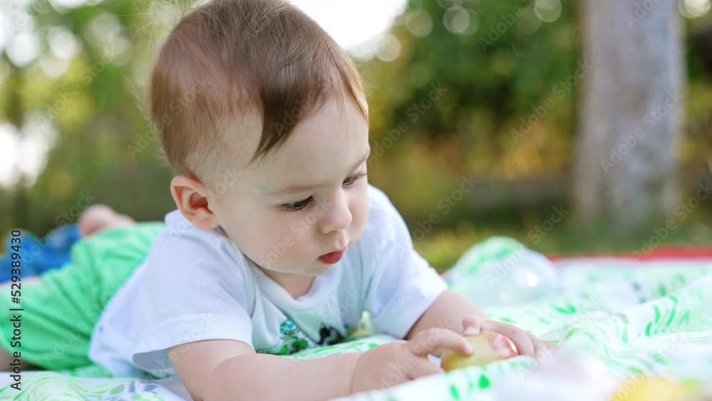 Lovely Caucasian child looking attentively at the apple. Nice cute boy lies on the grass in the garden in summer. Close up. Lovely Caucasian child looking attentively at the apple. Nice cute boy lies on the grass in the garden in summer. Close up.