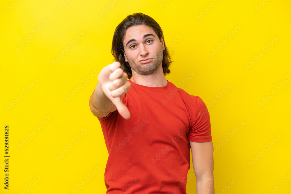 Caucasian handsome man isolated on yellow background showing thumb down with negative expression Caucasian handsome man isolated on yellow background showing thumb down with negative expression
