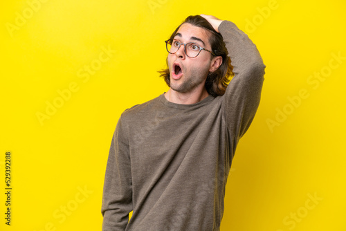 Caucasian handsome man isolated on yellow background doing surprise gesture while looking to the side © luismolinero