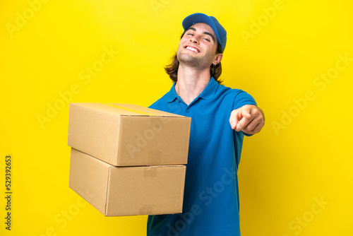 Delivery handsome man isolated on yellow background pointing front with happy expression