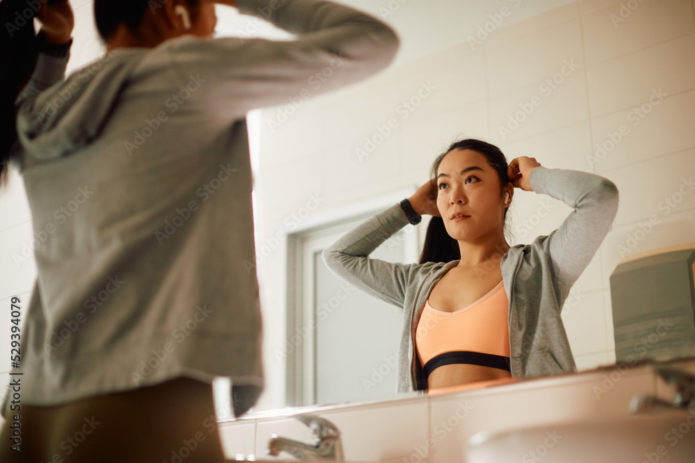 Asian athlete tying her hair in front on mirror before sports training in gym. Asian athlete tying her hair in front on mirror before sports training in gym.