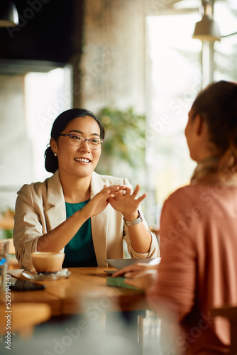 Happy Asian entrepreneur talks to her colleague during coffee break in cafe. photo