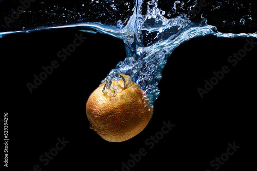 Kiwifruit dropped in water with splashes on black