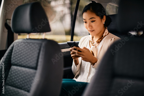 Asian female executive using smart phone while driving in car.