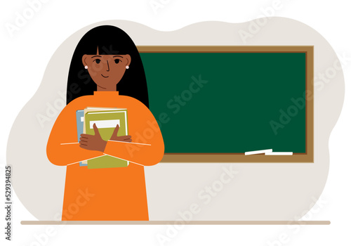 Female teacher with books on the background of the school board.