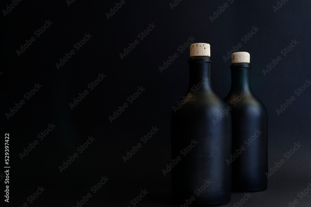 Black gin bottles, dark shot of two gin bottles with natural cork. The bottles are arranged on the right, so there is enough space for your text. Copy space for your design. Web banner. Black gin bottles, dark shot of two gin bottles with natural cork. The bottles are arranged on the right, so there is enough space for your text. Copy space for your design. Web banner.