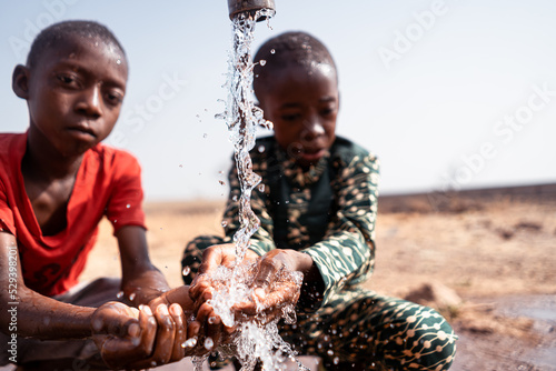 Fotografie Small malnourished African boys at a village well refreshing themselves; concept