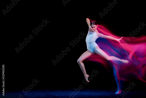 Young and graceful female ballet dancer dancing over dark background in mixed neon light. Art, motion, action, flexibility, inspiration concept. © master1305