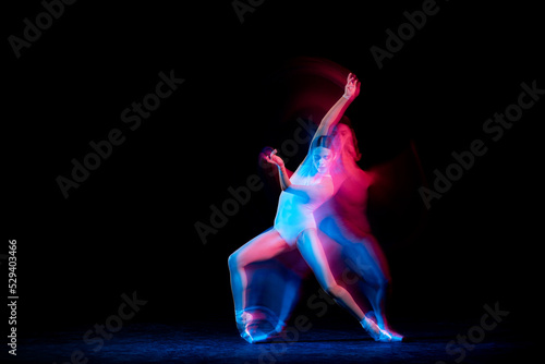 Graceful ballerina dancing on dark background in mixed neon light. Grace, movement, action and motion concept. Looks weightless, flexible.