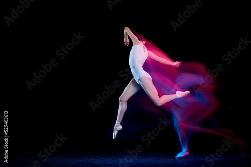 Graceful ballerina dancing on dark background in mixed neon light. Grace, movement, action and motion concept. Looks weightless, flexible.