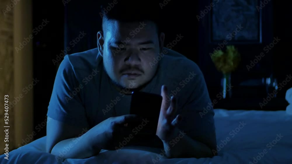 an asian man relaxing on the bed in bedroom and using mobile smart phone while laydown. an asian man relaxing on the bed in bedroom and using mobile smart phone while laydown.