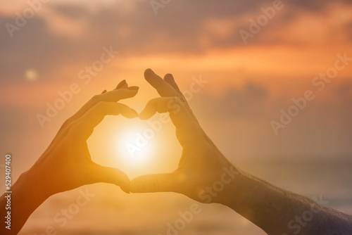 Silhouette hands of woman and man are lovely heart shape with sunset on through hand. Couple hands in heart shape with sunrise in middle and sea (ocean) background. Togetherness and love. Copy space