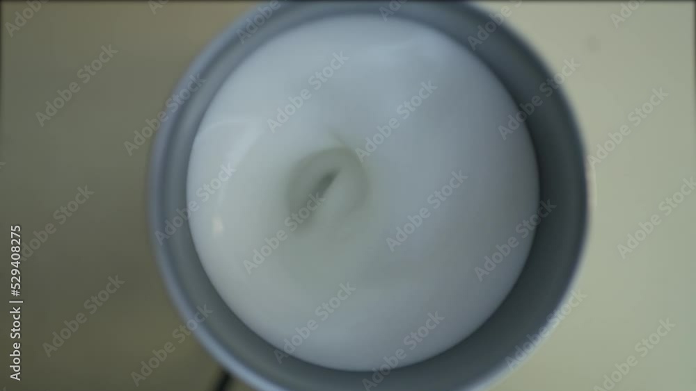 Top down perspective of household homemade milk frother while turning around to froth white milk causing bubbles and cream. Top down perspective of household homemade milk frother while turning around to froth white milk causing bubbles and cream.