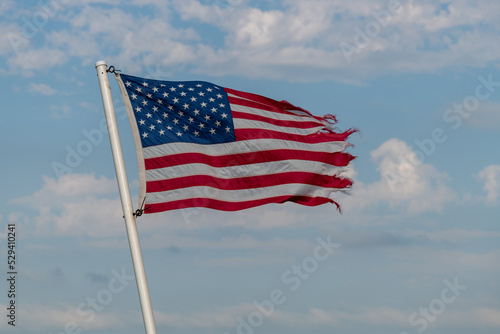 Canvas Print Tattered American flag against blue sky with white clouds in rural Minnesota USA