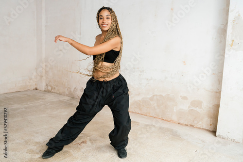 girl with long blonde braids dancing in a black tracksuit in an abandoned warehouse while smiling and enjoying her passion and exercise. © Beatriz