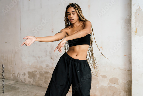 girl with long blonde braids dancing in a black tracksuit in an abandoned warehouse while smiling and enjoying her passion and exercise.