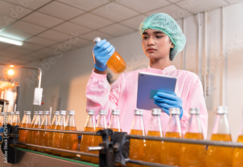 Inspector woman use tablet checking bottle juice with glass bottle product and machine at food industry	 photo