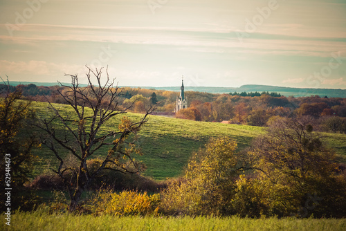 Clocher d'une église apparaissant à l'arrière-plan d'un paysage vallonné aux couleurs d'automne